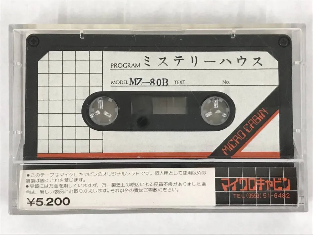 ケースに入った『ミステリーハウス』のカセット。白いラベルに PROGRAM「ミステリーハウス」、MODEL「MZ-80B」。右下の斜めの黒い帯に、赤い字で「MICRO CABIN」。ケースの下の帯に「¥5,200」と、黒地に赤い「マイクロキャビン」と電話番号